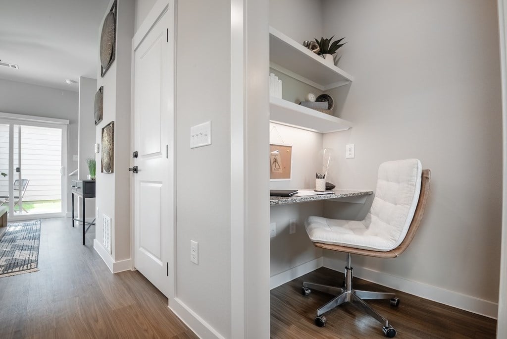 A white chair is in front of a desk with a shelf above it.