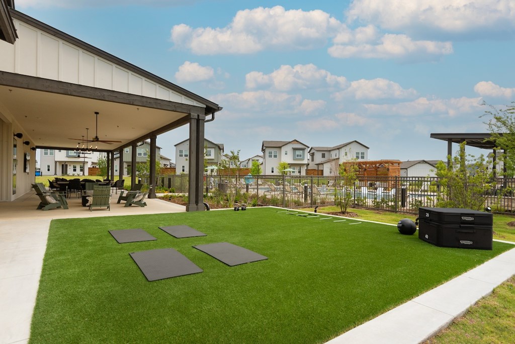 A covered patio area with a green lawn and a black trash bin.