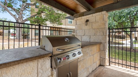 an outdoor kitchen with a grill and a bar with stone walls and a fence