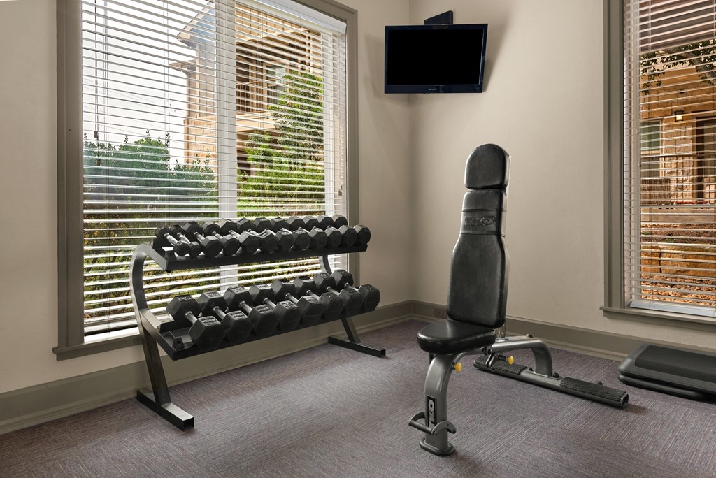 a fitness room with a chair and dumbbells and a television