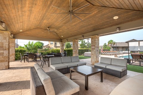 a covered patio with couches and tables and a pool