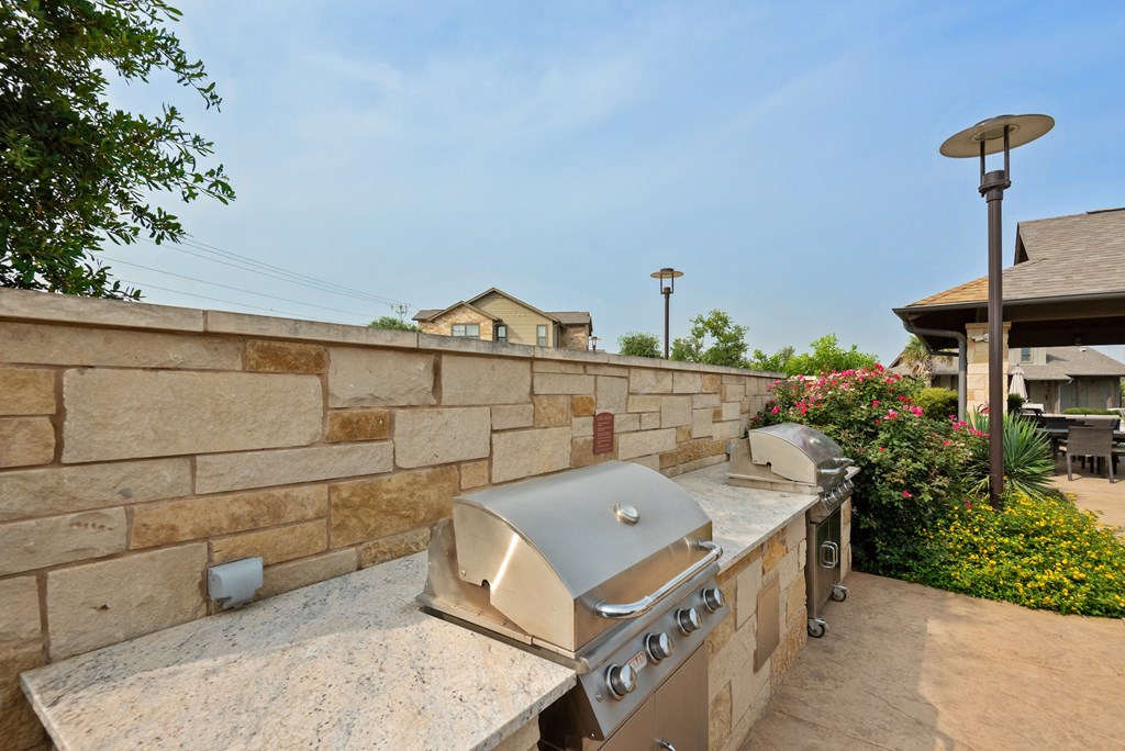 an outdoor kitchen with a stone wall and a grill