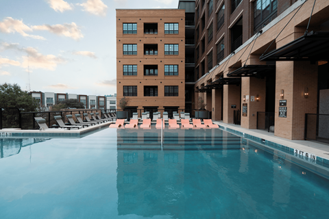 A large swimming pool in front of a building with lounge chairs around it.