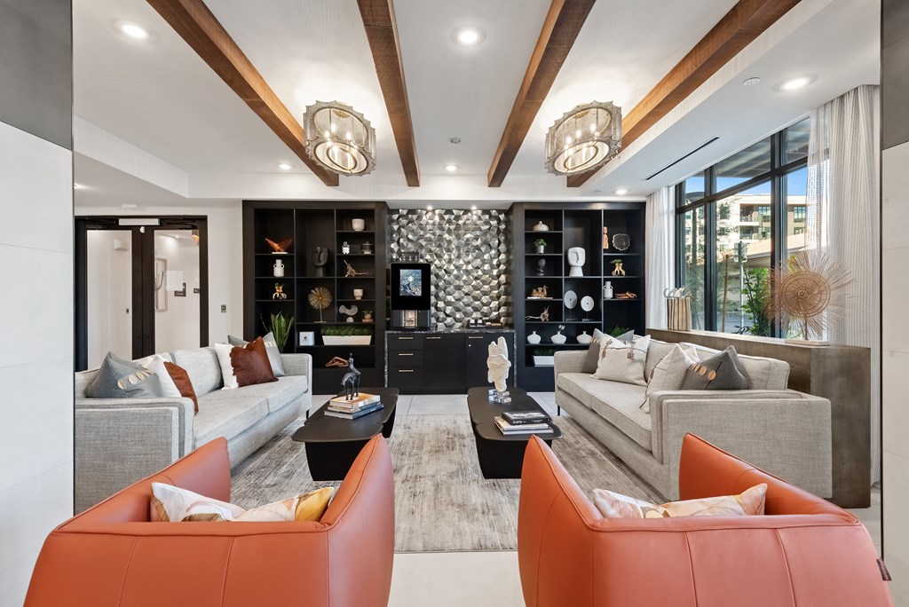 A modern living room with a grey sofa, orange chairs and a black bookshelf.