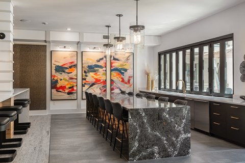 a long kitchen with a marble counter top and chairs