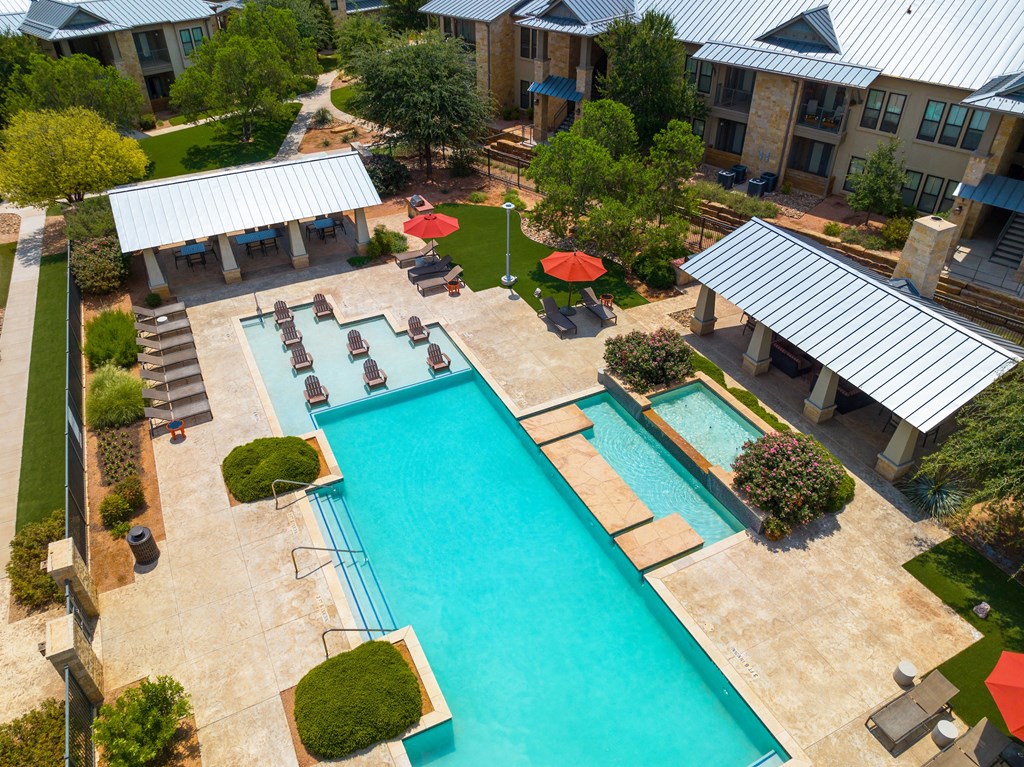 an aerial view of a resort style pool with lounge chairs and umbrellas