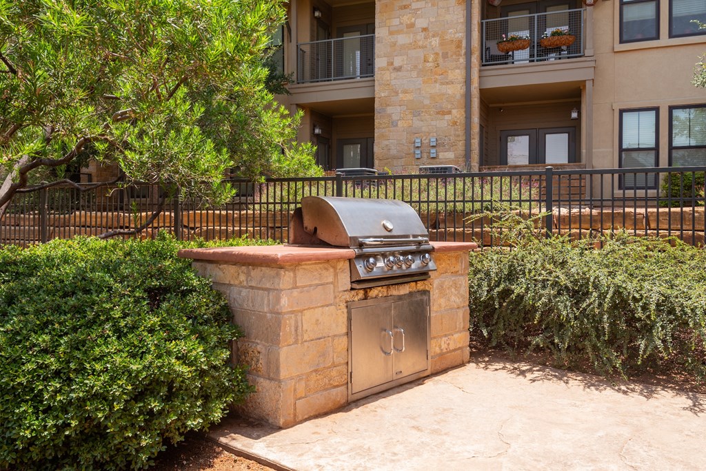 an outdoor barbecue grill with a stone countertop in front of an apartment building