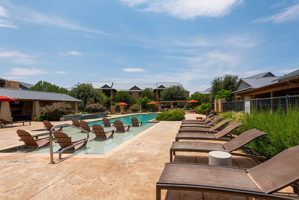 a pool with lounge chairs and umbrellas at the whispering winds apartments in pearland,