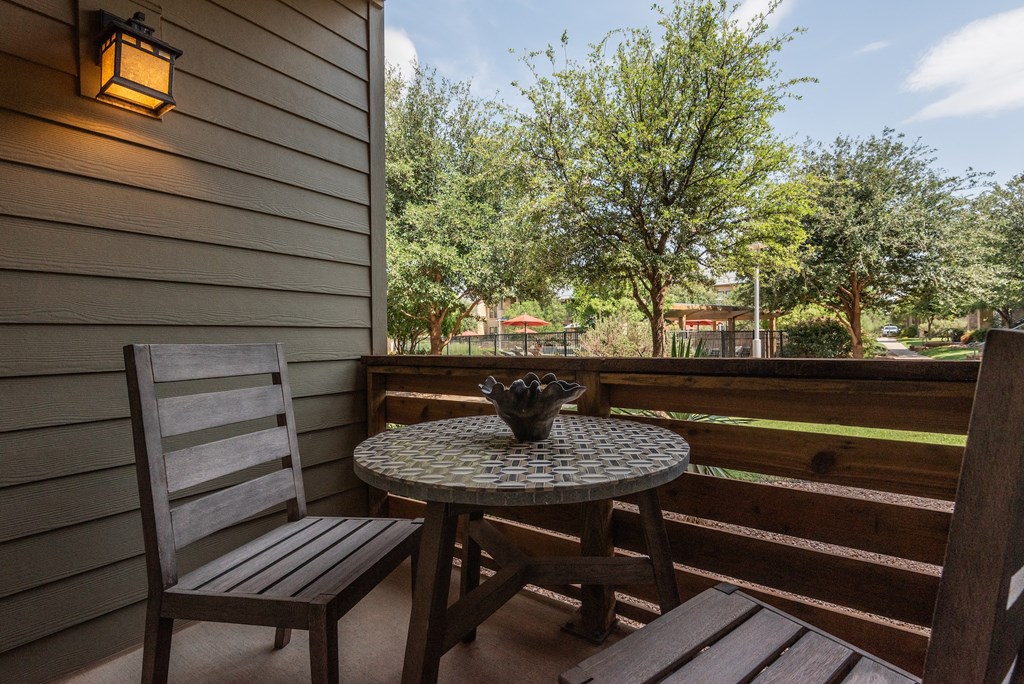 a table and two chairs on a balcony with trees in the background