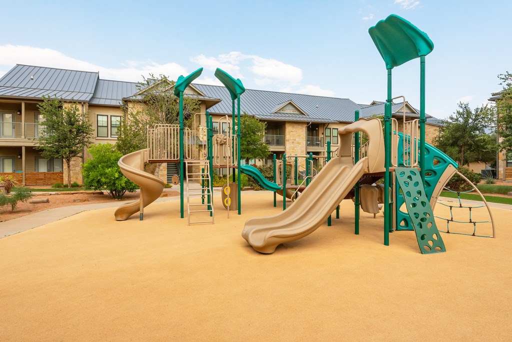 a playground with two slides and a climbing structure in front of an apartment building