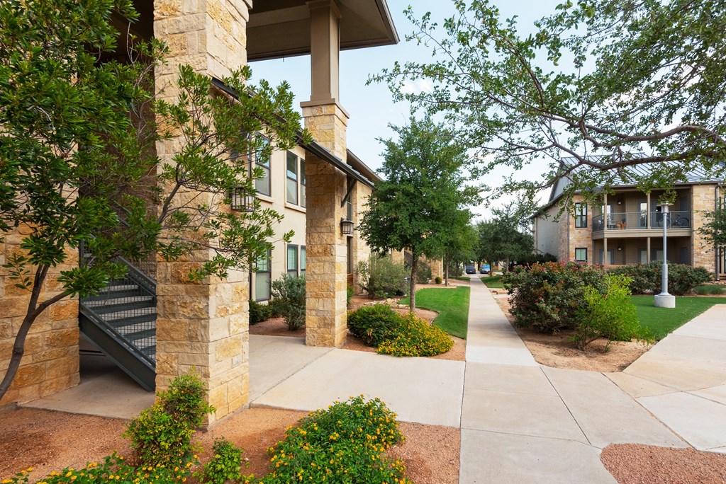 a walkway with trees and bushes in front of a building