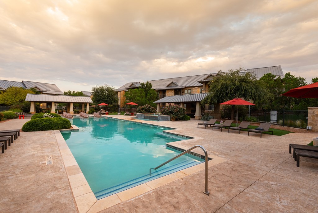 a swimming pool with lounge chairs and umbrellas in front of a building