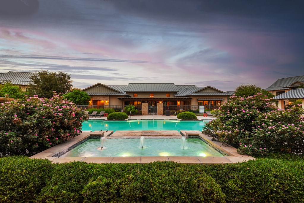 a large swimming pool surrounded by bushes and trees with a building in the background
