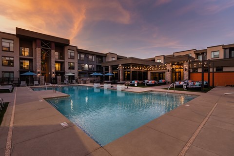 A swimming pool in front of a building with lights on.