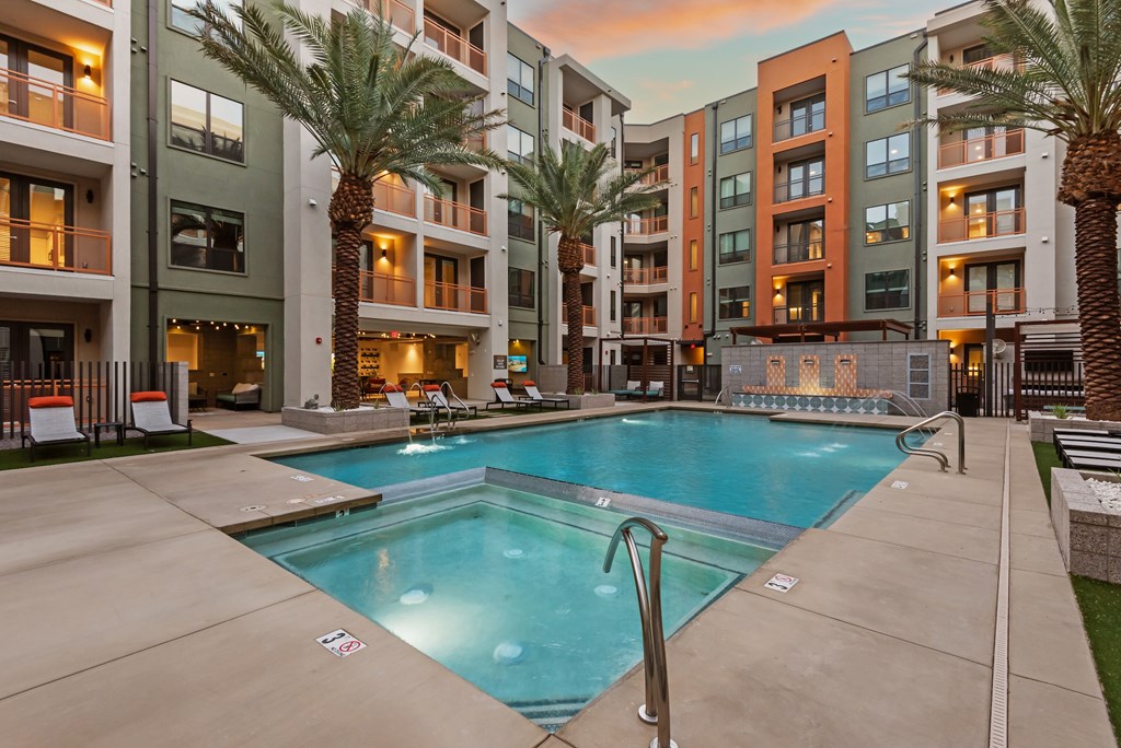 A swimming pool in front of apartment buildings with palm trees.