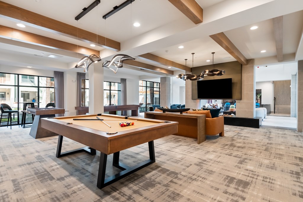 A billiard table is in the middle of a room with a bar and a television.