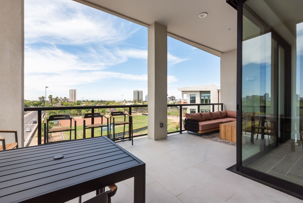 A balcony with a table and chairs overlooking a tennis court.