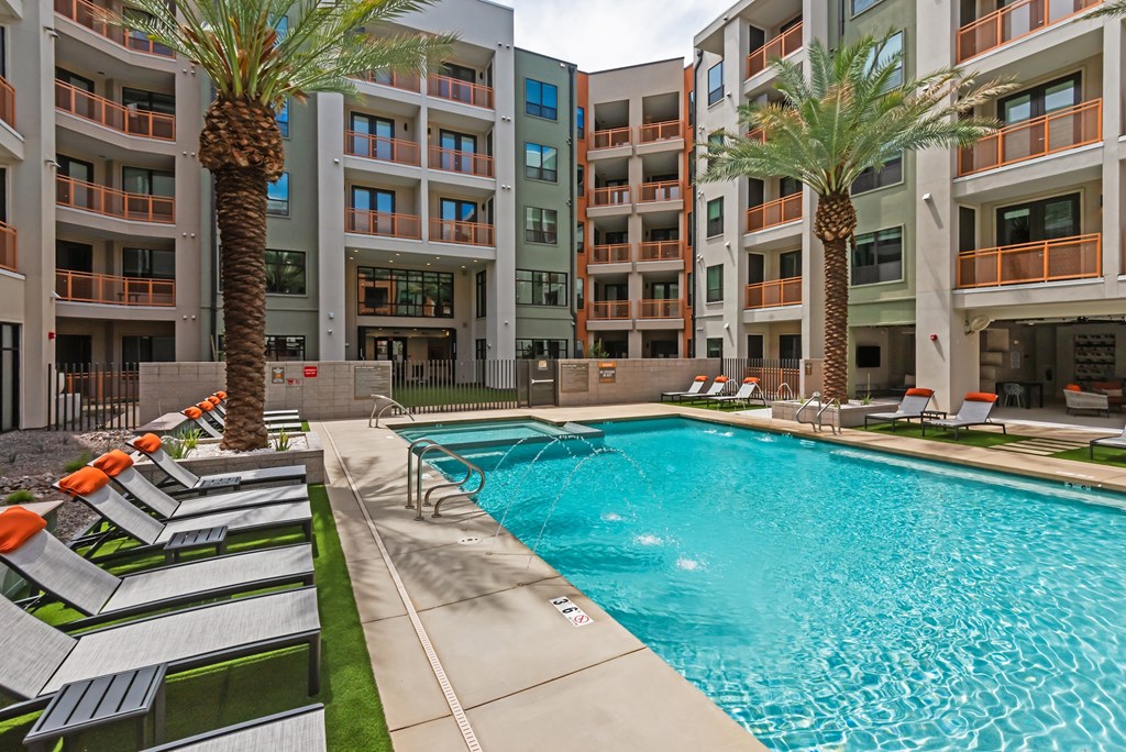 A swimming pool surrounded by palm trees and lounge chairs in front of apartment buildings.