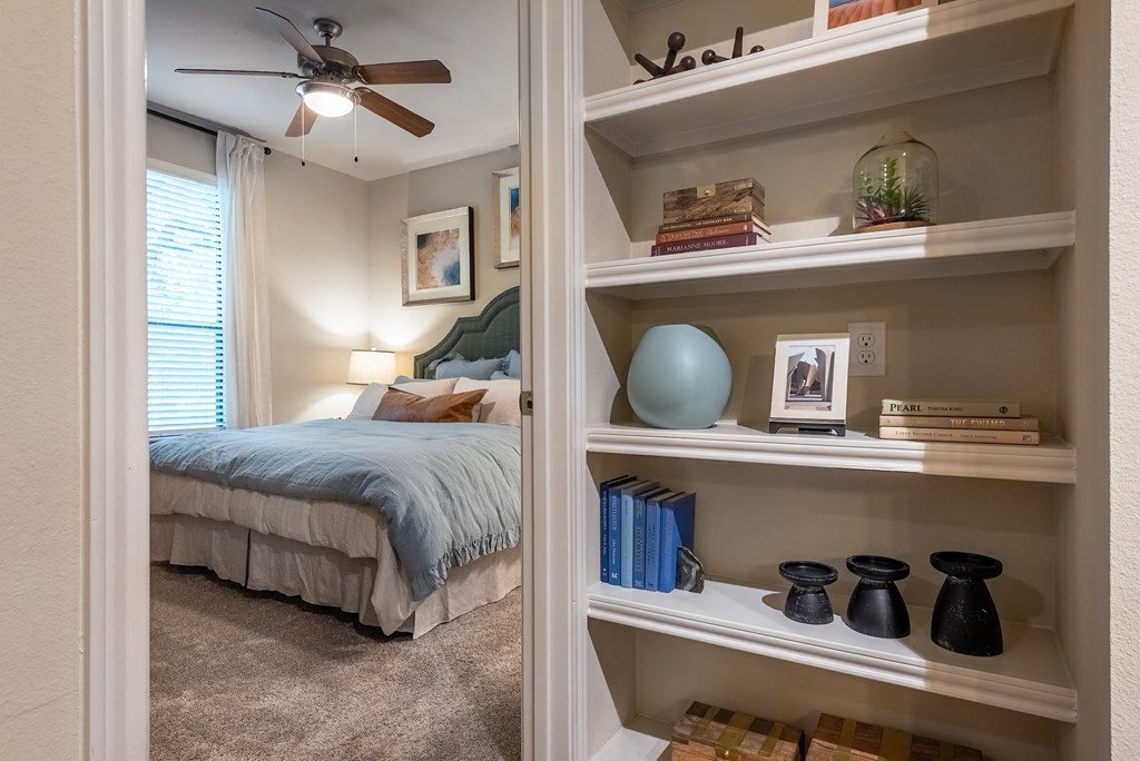 a bedroom with a bed and shelves with books and a ceiling fan