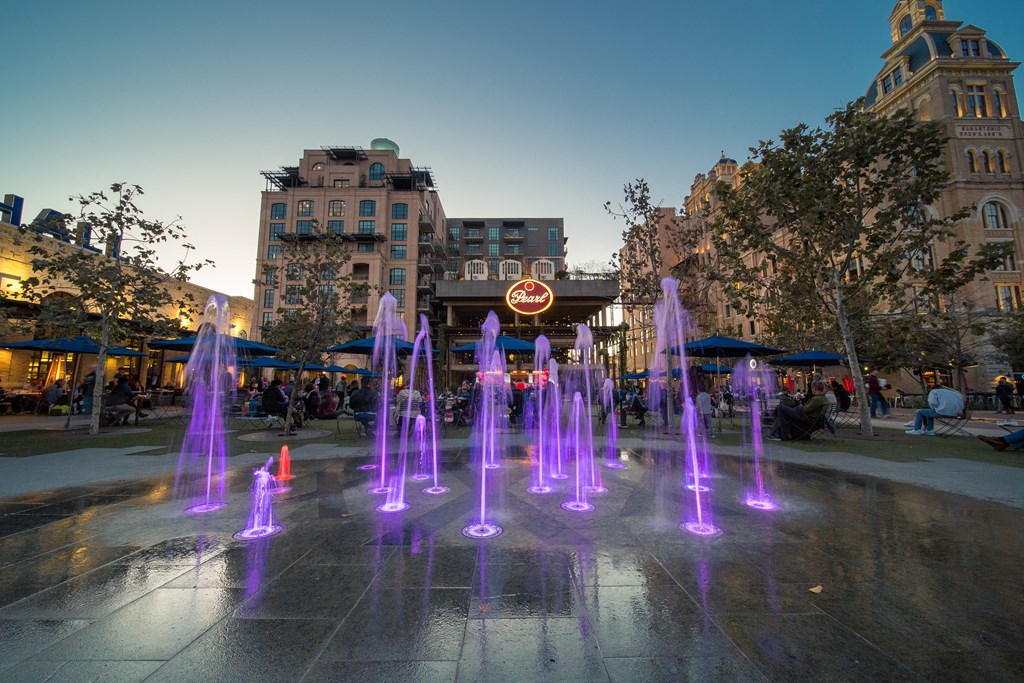 A fountain with purple lights in the middle of a city square.