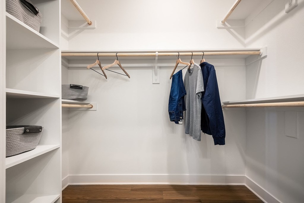 a walk in closet with white walls and wood floors
