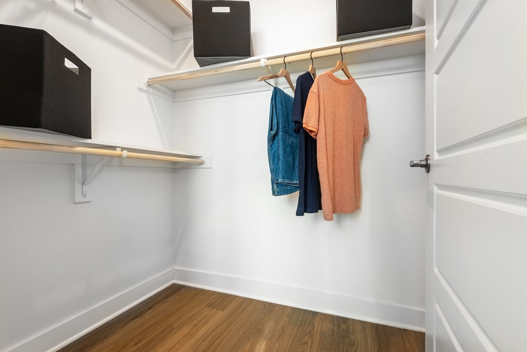 a walk in closet with white walls and wood floors