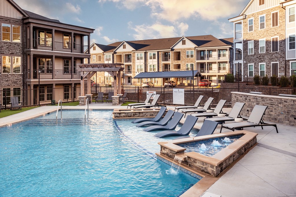 a swimming pool with lounge chairs in front of an apartment building