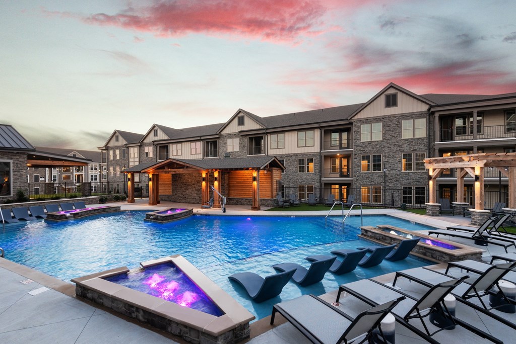 a large swimming pool with lounge chairs in front of an apartment building