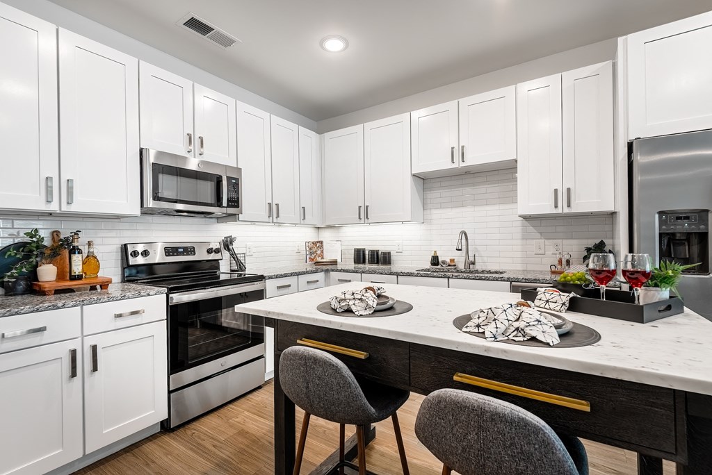 a kitchen with white cabinets and a large island with two chairs