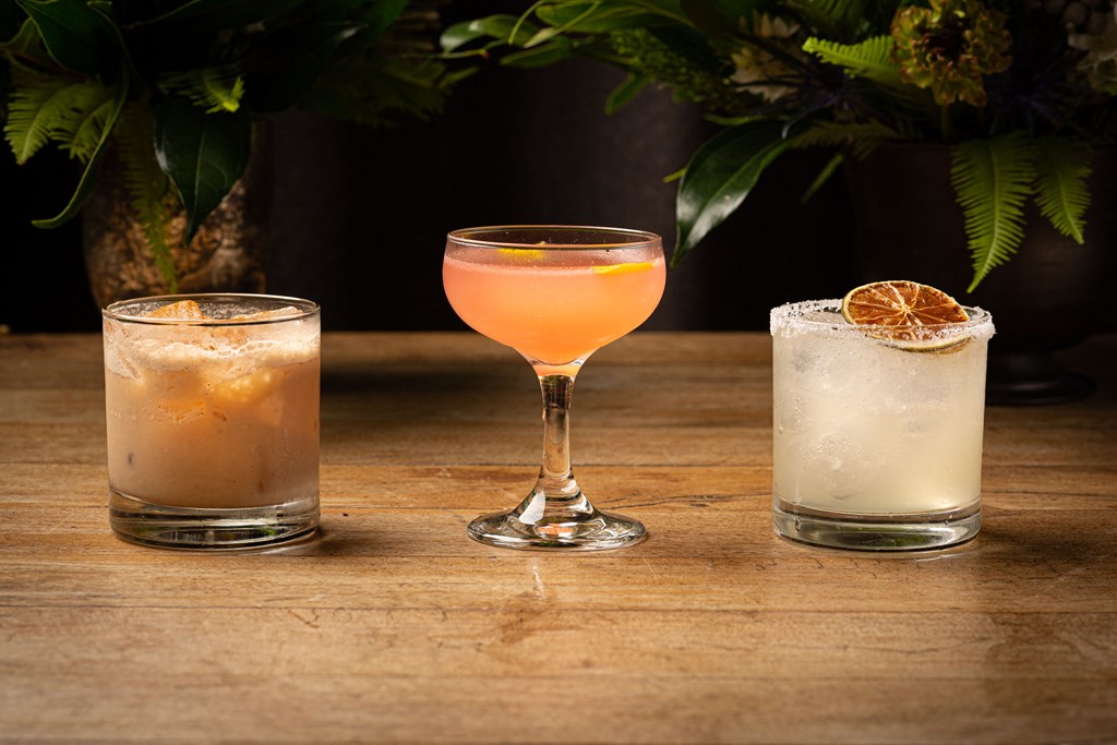 Three different cocktails are displayed on a wooden table.