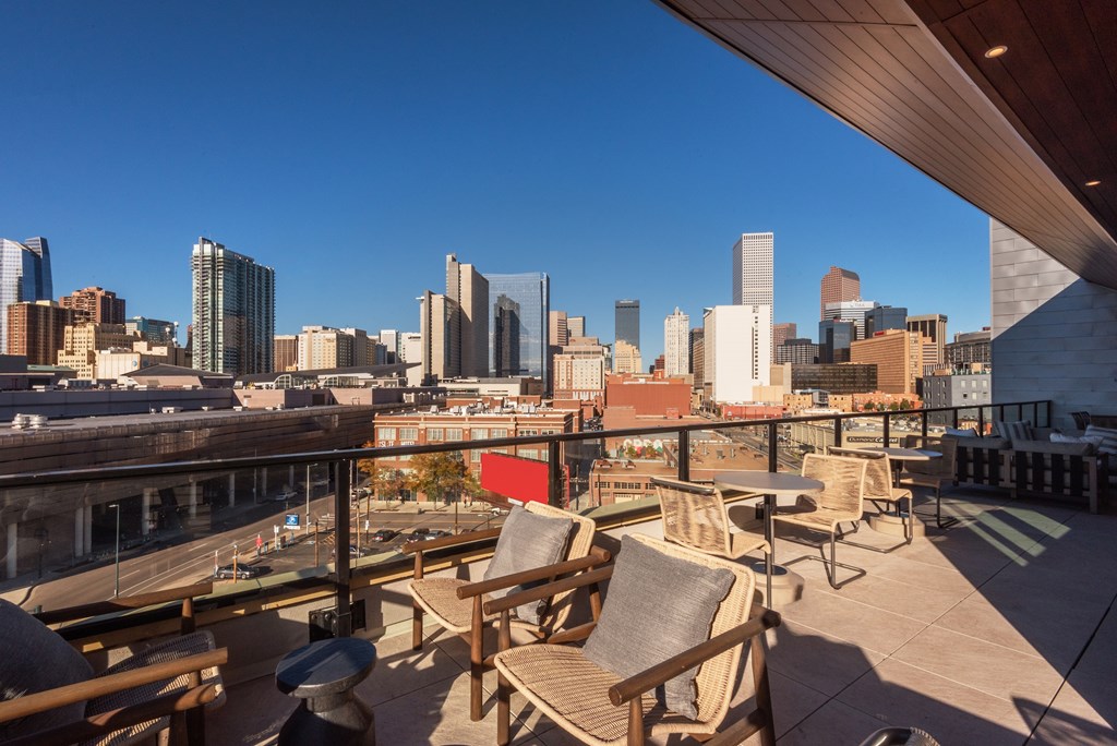 A rooftop patio with wooden furniture overlooking a city skyline.