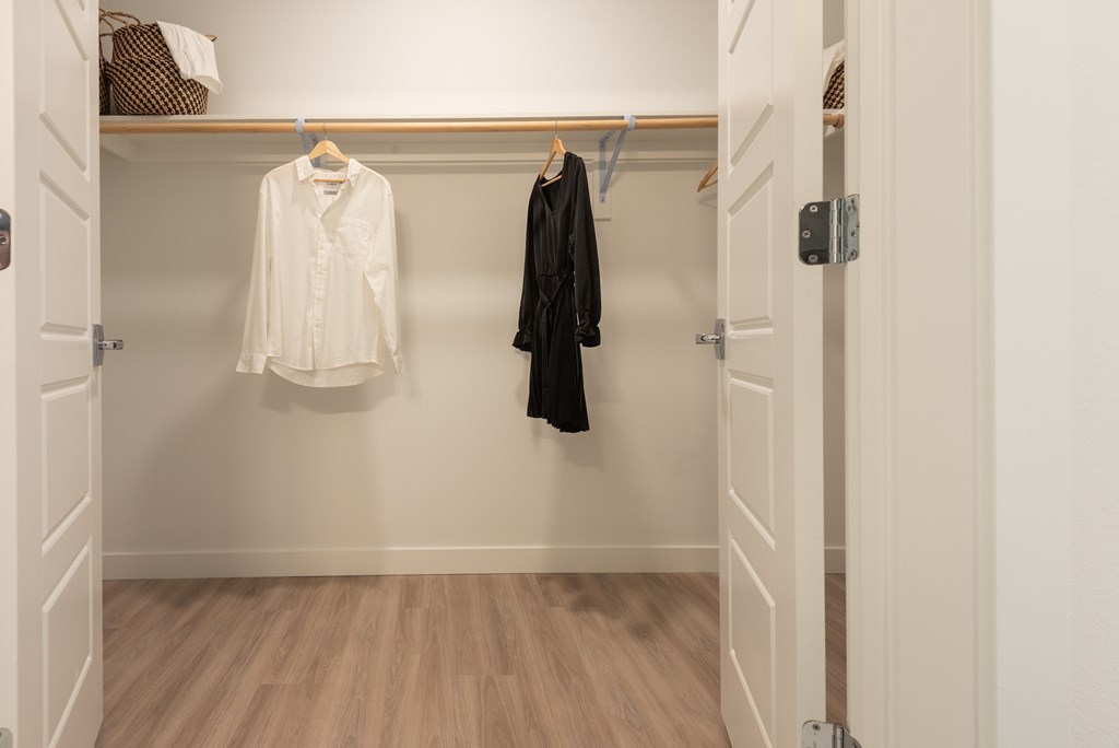 A white shirt and a black jacket are hanging on a wooden hanger in a white closet.