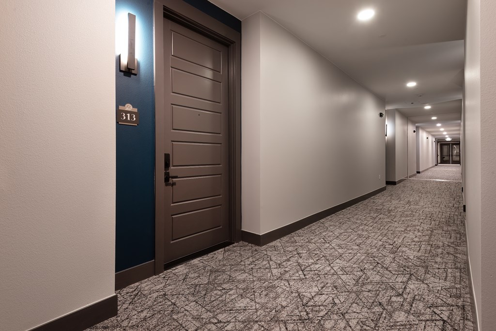 A hallway with a blue door and a carpeted floor.
