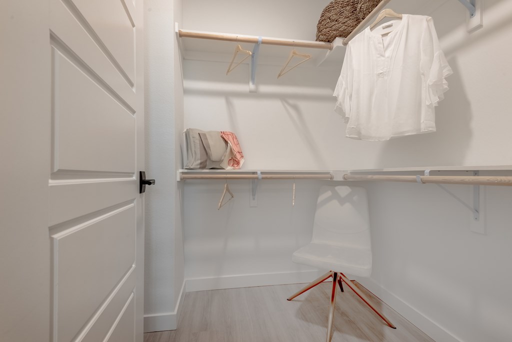 A white closet with clothes hanging on hangers.