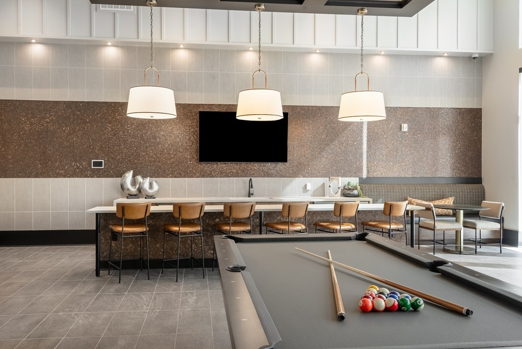 A billiard table with balls and cues is in the middle of a room with chairs and a television.