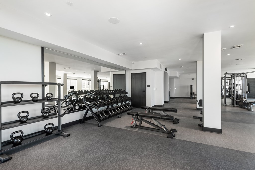 A gym with a variety of equipment including kettlebells, weight machines, and a bench press.