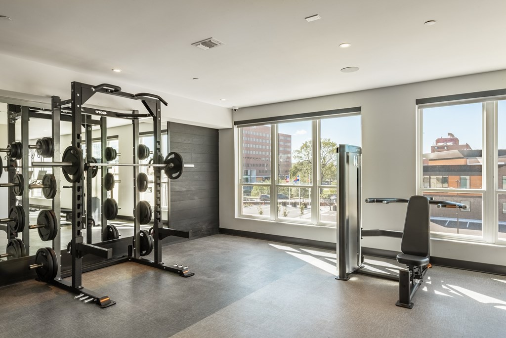 A gym with a weight rack, bench, and windows.