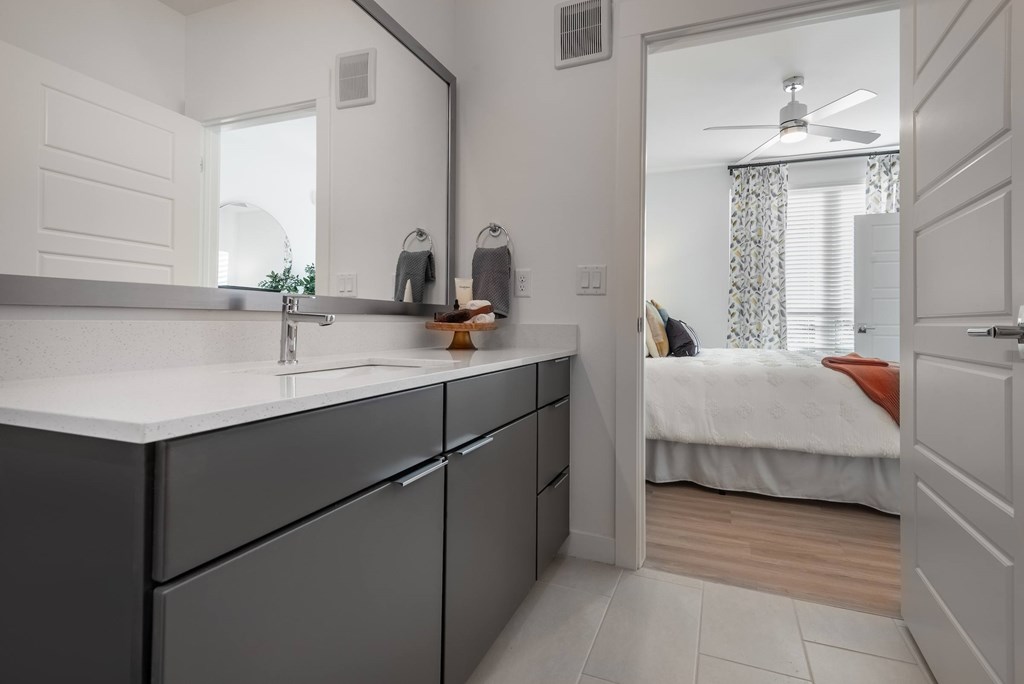 A bathroom with a sink, mirror, and a bedroom in the background.