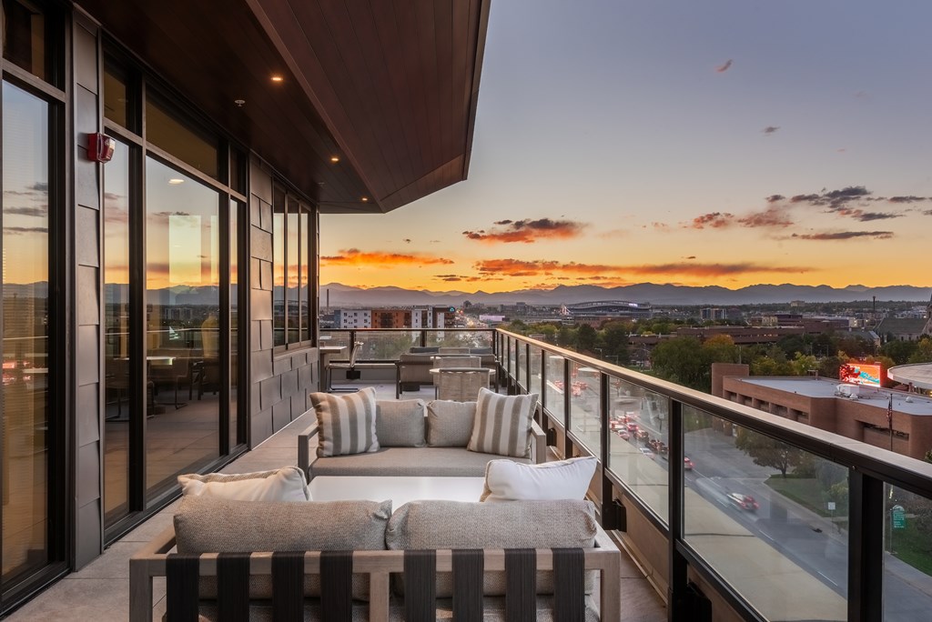 A balcony with a couch and pillows overlooks a cityscape at sunset.