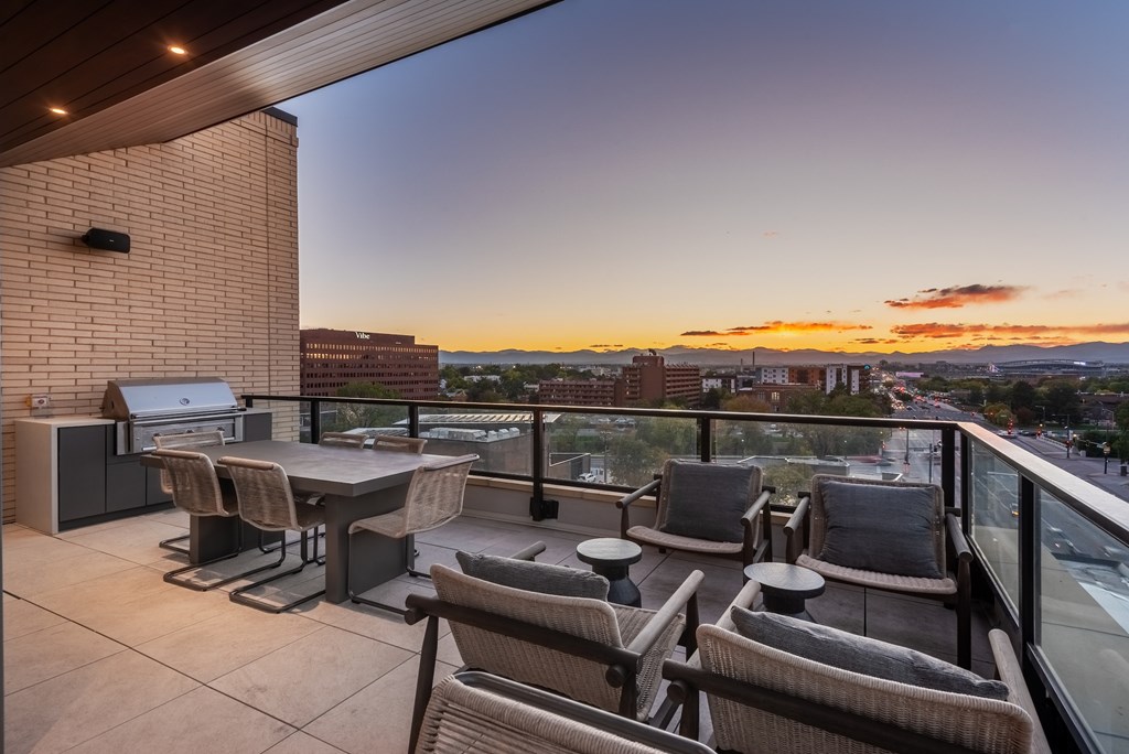 A patio with a table and chairs overlooking a cityscape at sunset.