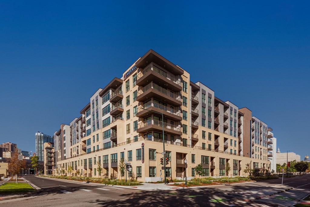 A large, modern building with many windows and balconies is situated on a street corner.