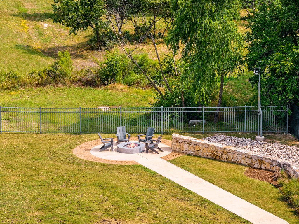 a fire pit in the middle of a grassy area with chairs and a stone wall