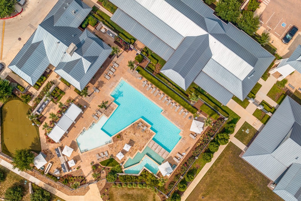 a birdseye view of a large swimming pool surrounded by houses with grey roofs