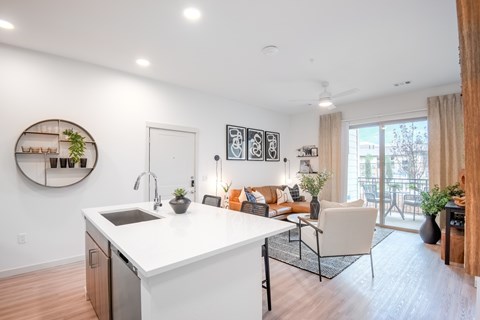 A modern kitchen with a white countertop and a dining area with a couch and chairs.