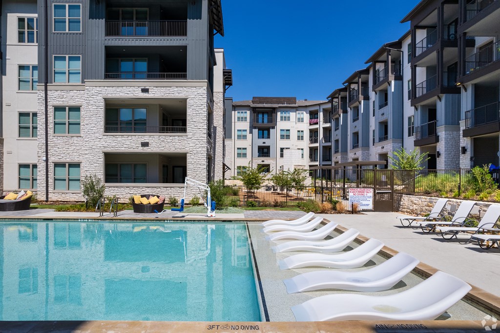 an outdoor pool with white chairs and an apartment building in the background