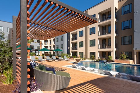 a large pool with chairs and umbrellas in front of an apartment building