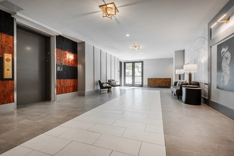 the lobby of a condo with a large white tiled floor and a glass door