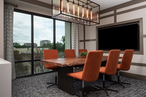 a conference room with a large screen tv and a wooden table with orange chairs