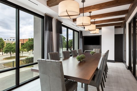 a long dining table with chairs and a television in a room with large windows