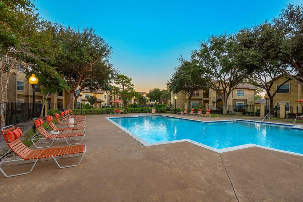 A swimming pool surrounded by orange chairs and trees.